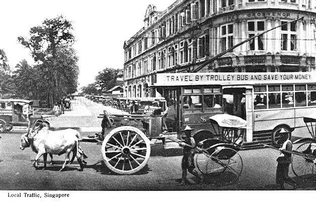 Traffic scene at the junction of Stamford Road and Hill Street, Singapore, showing an early advertisement by Singapore Traction Company on its trolley bus. The Oranje Building (later renamed Stamford House) stands in the right background.