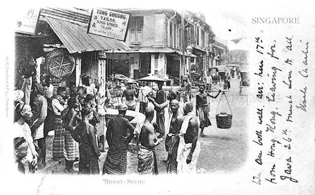 A gathering of street hawkers and others in front of Tong Cheong Tailor at the junction of South Bridge Road and Cross Street in Chinatown, Singapore. Cross Street was a busy street in the city popular for its many street shows and shops. Although in Chinatown, the district between Cross Street and the nearby Chulia Street was home to a substantial Indian community. The image reflects the multi-ethnic nature of Singapore society.