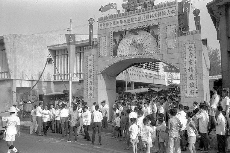Crowd gathering around the welcoming arch at Lim Tua Tow Market, located off Upper Serangoon Road, during Prime Minister Lee Kuan Yew's tour of Serangoon Gardens Constituency