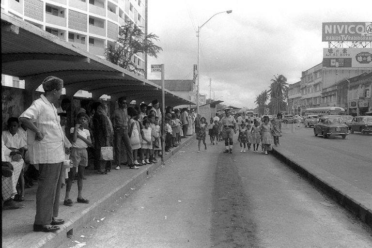 This street is located along Changi Road (direction towards Changi). Bus-stop was in front of Block 2, Jalan Pasar Baru (originally Jalan Geylang Serai), where Geylang Serai Market / Food Centre currently is. Part of the structure of the Taj Cinema (renamed Singapura) can be seen in the background.