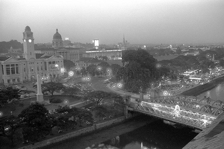 Night view of Anderson Bridge over mouth of Singapore River in the foreground, with Dalhouise Obelisk, Victoria Memorial Hall and Elizabeth Walk (Esplanade Park). On the right is the Singapore Food Carnival, organised by Tourist Promotion Board as part of Tourist Week from 26 to 28 September, held at Satay Club in Elizabeth Walk. Visible in the background is Supreme Court (with dome).
