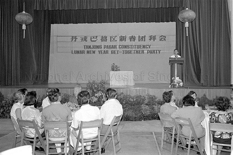 Host of the Lunar New Year get-together party delivering welcome address at Tanjong Pagar Community Centre. Prime Minister Lee Kuan Yew and wife are seated at the table on the left.