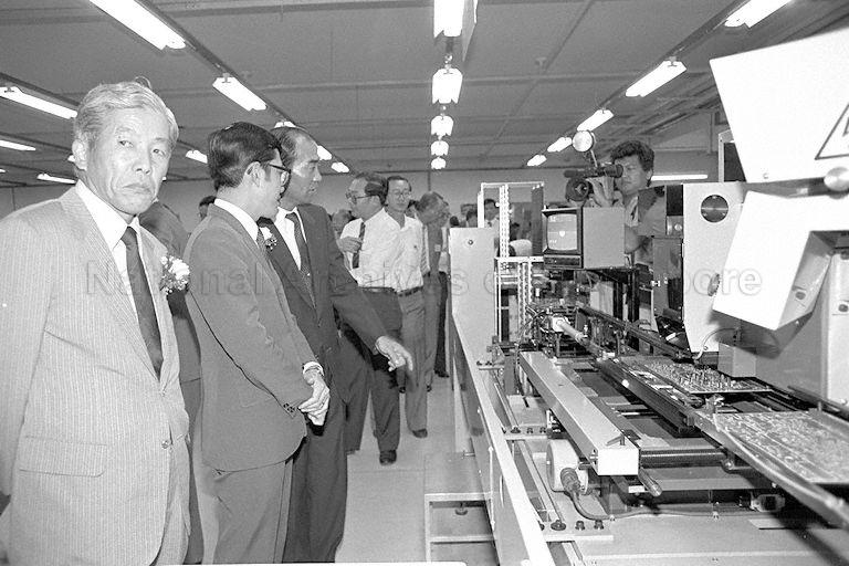 Labour Minister Lee Yock Suan being briefed by an official during his tour of Aiwa's manufacturing plant in Jurong. Two of the company's newest products, its digital audio tap (DAT) system and the 8 millimetre video camera recorder, are demonstrated at the plant opening. On the left is Aiwa Co Deputy President Hajime Unoki.
