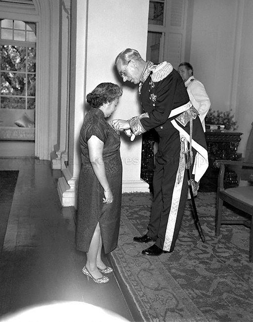 Mrs Helen Tan Chin Tuan, wife of Deputy President of Legislative Council, being given the MBE (Member of the British Empire) by His Excellency the Governor Sir John Nicoll at an investiture held at Government House