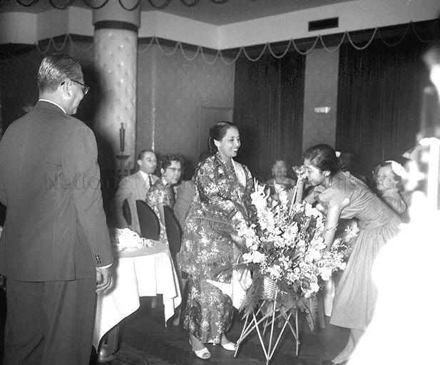 Puan Sharifah Rodziah, wife of Federation Prime Minister Tunku Abdul Rahman (looking on, left), being presented with floral basket when they arrive from Ceylon by the ship S S Cambodge