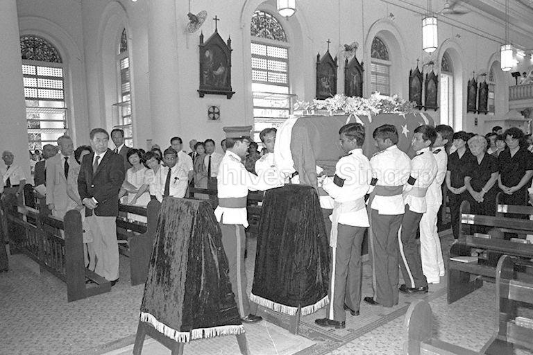 The casket of the late Minister for Finance Hon Sui Sen is brought into the Cathedral of the Good Shepherd by eight Singapore Armed Forces (SAF) men followed by Mrs Annie Hon and daughters (in black). The acting President Dr Yeoh Ghim Seng, Prime Minister Lee Kuan Yew and First Deputy Prime Minister Dr Goh Keng Swee head the list of dignitaries at the funeral service. Also present are a number of Mr Hon's Cabinet colleagues, junior ministers, Members of Parliament (MPs), top civil servants, diplomats, other VIPs and several Catholic nuns and brothers.