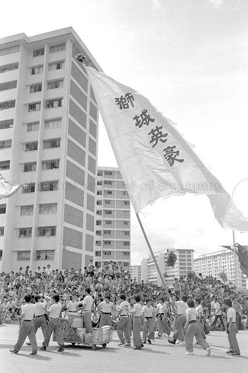 Performers balancing giant flag, bearing Chinese words "ç‹®åŸŽè‹±è±ª" (Heroes of the Lion City), with acrobatic acts during Chingay procession at Ang Mo Kio