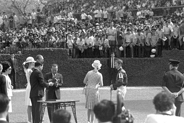 Queen Elizabeth II (back to camera) presenting a gold-mounted whip to Lester Piggott, English jockey of the winning horse of Queen Elizabeth II Cup, at Singapore Turf Club in Bukit Timah. Looking on are (from right to left) club chairman Tan Sri Runme Shaw, Duke of Edinburgh Prince Philip, Princess Anne and Mrs Shaw.