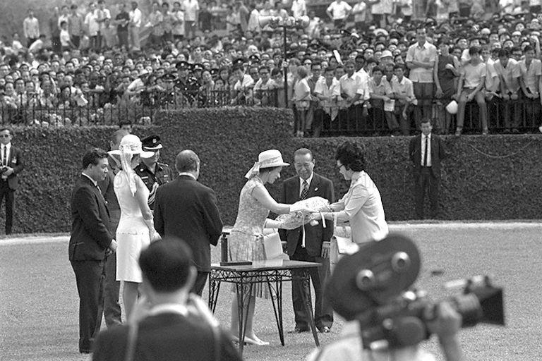 Queen Elizabeth II receiving a bouquet of flowers from wife of Chairman of Singapore Turf Club Mrs Runme Shaw, after presenting prizes of the Queen Elizabeth II Cup. Looking on are (from right to left) Runme Shaw, club secretary D R H Brown (back to camera) and Princess Anne.