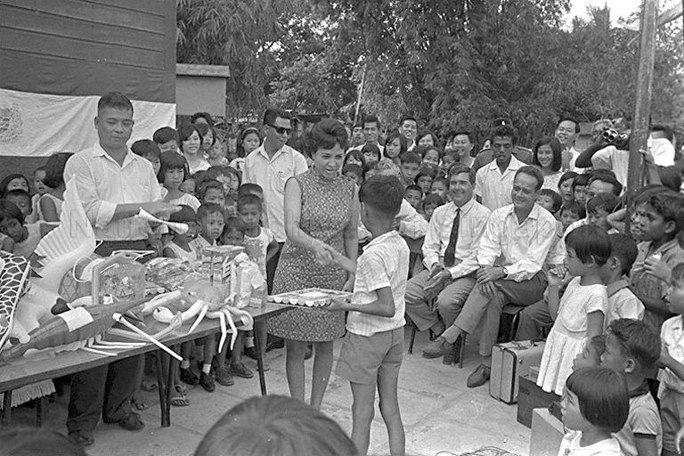 Mrs Gloria Barker presenting gifts to children during Hari Raya Puasa and Chinese New Year party at Kampong Chantek Lama Community Centre at Whitley Road. Seated on the right is Minister for Law and National Development E W Barker.