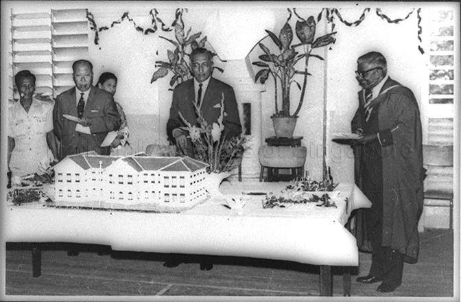 Yang Di-Pertuan Negara of Singapore Yusof Ishak cutting cake, in the shape of the school building, at Raffles Institution's 141st anniversary and Founder's Day celebration. Standing on the right is Principal E W Jesudason.