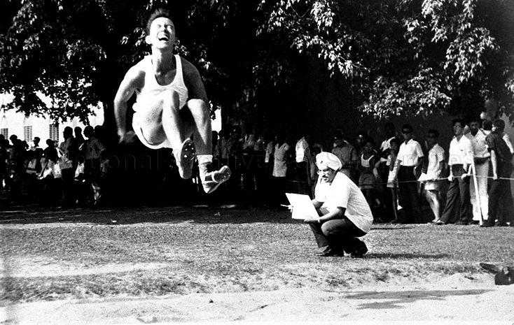 Competitor Victor Lye doing the long jump, watched by field judge Charan Singh