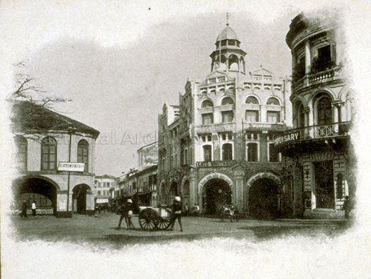View of northwest corner of Raffles Place, formerly known as Commercial Square, at junction of Kling Street (later known as Chulia Street) and Bonham Street. The ornate building on the right is Bonham Building and on the extreme right is the Dispensary building.