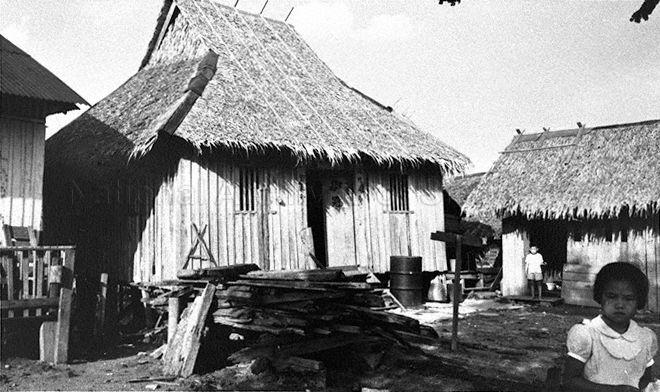 Traditional Chinese-style kampong houses with sloping thatched roof and timber plank walls in Kallang Basin. The containers placed outside the house under the roofline might have been used to collect roof drips on a rainy day.