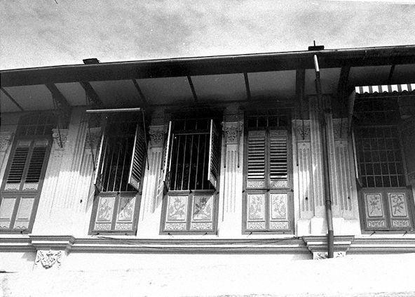View of three sets of windows on upper storey of a Peranakan shophouse. Windows are segmented so that lower section can remain shut to maintain privacy for the occupants. Vertical bars spanning the length of windows provide added security.