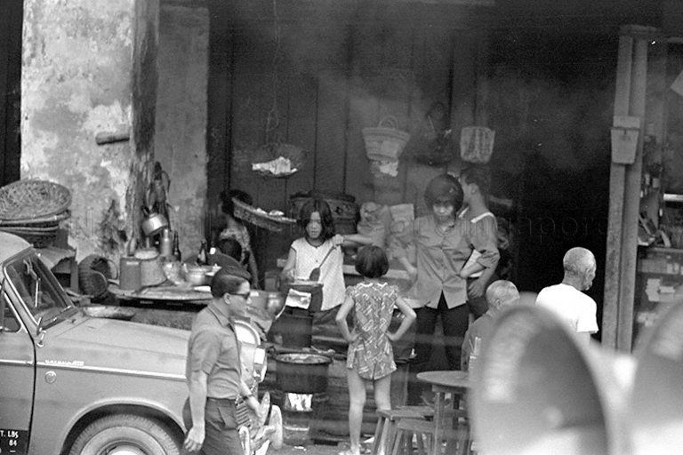 This is a street hawker operating from a "five- foot-way".  Customers sit at the wooden table which has all the eating utensils placed in a container and food seasoning comprising soya sauce and chilli in small bottles.