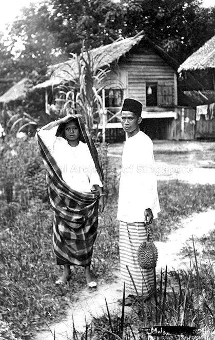 Malay couple in a village, Singapore. The Malay man is holding a durian, a thorny tropical fruit.