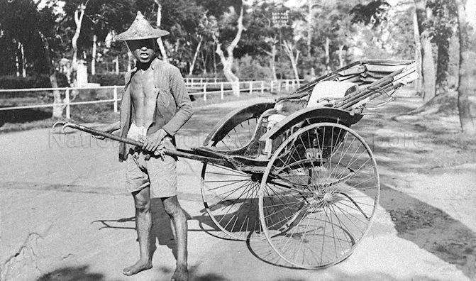 A rickshaw puller wearing a large straw hat pulling his rickshaw