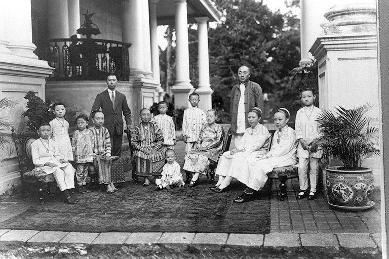 Group photograph of Tan Soo Bin (man standing on the right) and family taken at his residence, the Panglima Prang in Jalan Kuala off River Valley Road. Tan Soo Bin is the eldest son of Tan Jiak Kim and great-grandson of Tan Kim Seng who built the bungalow before 1860 . The brass fountain in the background (left) was a gift to Tan Jiak Kim from businessmen and community leaders.