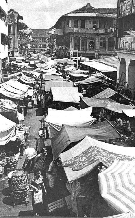 People patronizing the market stalls at Trengganu Street and the junction of Smith Street in Chinatown. Building at this junction is the former Lai Chun Yuen Opera House.