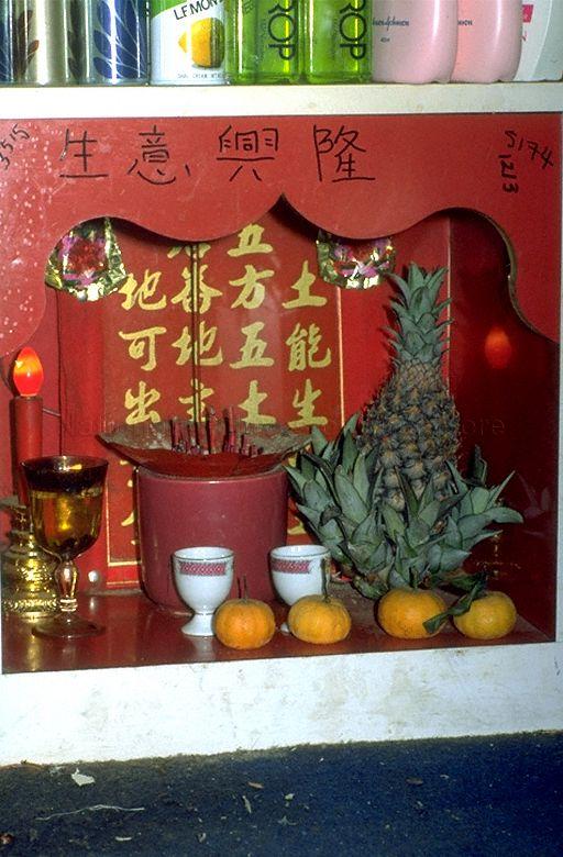 Chinese altar in a shop in Chinatown with offerings of incense, pineapple and mandarin oranges. Chinese characters in black on the top of the altar express a wish for success in business.