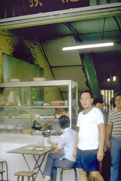 This is a photo of the shophouse at 126-A, Albert Street (road expunged). It was a rented property which housed Ng Teck Huat (黄德发), a bak kut teh shop run by Ng Wei Chian's Teochew grandparents, Ng Ah Liang (d. 1946) and Tay Gim Ching (1910 - 2001), who immigrated to Singapore in 1918 from the village of Gek Poh (Yupu), near the city of Jieyang in the Chaoshan region, Guangdong province, China.<br /><br />They started selling bak kut teh and Teochew porridge from this shophouse around 1936, and the business continued until 1990, when the land was given up for redevelopment (the site is currently part of LASALLE College of the Arts). They had eight children, and the entire family lived on the second floor of the shophouse (the staircase on the left of the photo led upstairs).<br /><br />The man in a white T-shirt facing the camera is Ng Wei Chian's second paternal uncle, Ng Seow Khern (d. 2001). He was the main cook in the business, and following the shop's closure, continued selling bak kut teh from a stall in a coffeeshop opposite the shophouse.<br /><br />An interesting point was that while Ng Wei Chian's paternal family is Teochew, they sold Hokkien-style bak kut teh, which is much darker than the clear, Teochew-style bak kut teh more commonly found in Singapore. The story is that Ng Wei Chian's grandfather learnt the recipe from a Hokkien friend.