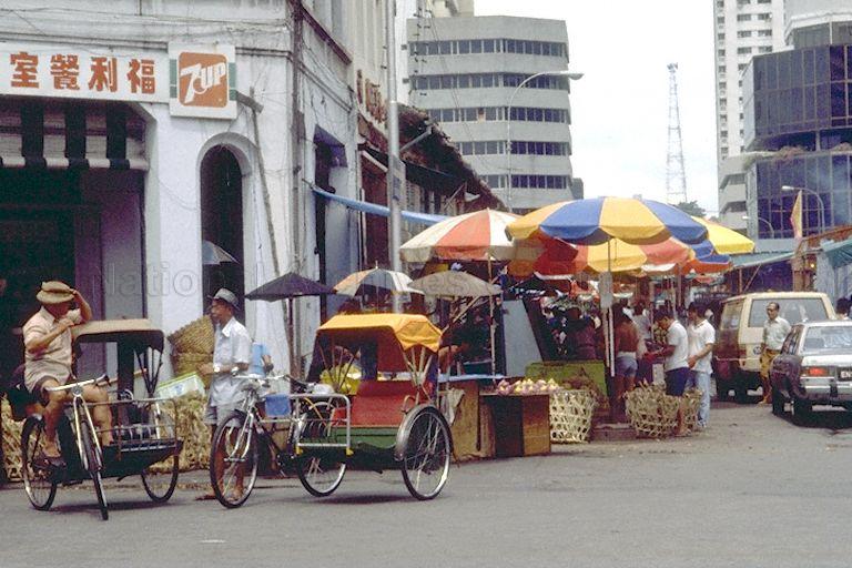 View of trishaw riders and fruit stalls at Queen Street before Middle Road junction. On the right is Midlink Plaza.