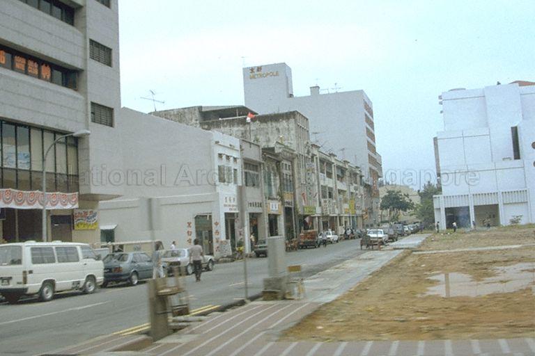 Seah Street towards Beach Road, with Metropole Hotel and faÃ§ade of Beach Road Camp afar (partially hidden by a tree)