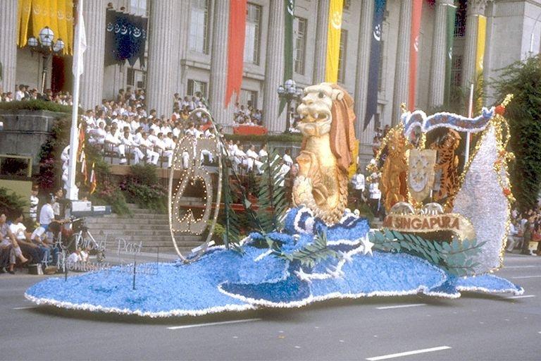 National Day Parade 1984 at the Padang -- Singapore Tourist Promotion Board (STPB) float moving past City Hall. The gold Merlion was part of the STPB/Singapore Airlines (SIA) float which was designed by Donald Bent and had earlier won a prize at the Pasadena Rose Parade in California.