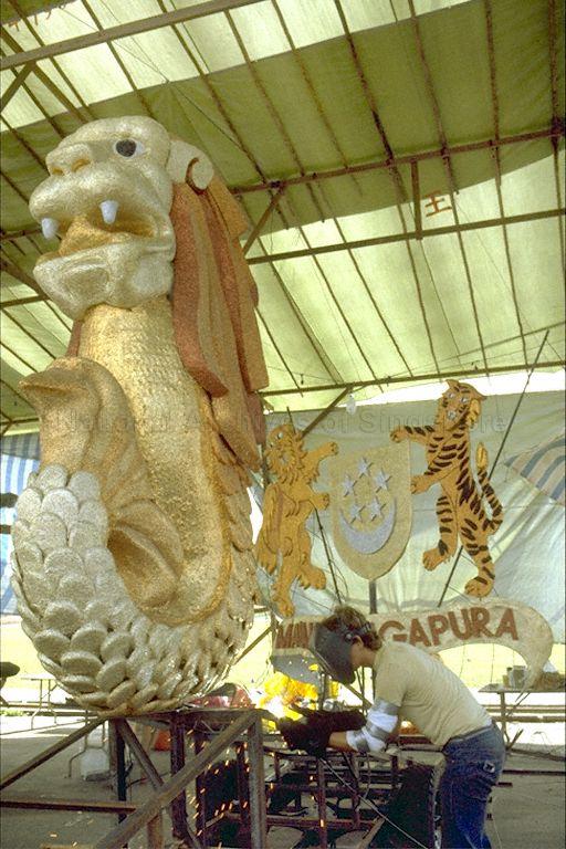 National Day Float Procession 1984 -- View of gold Merlion on the Singapore Tourist Promotion Board (STPB) float being prepared at the Air Movement Centre at Paya Lebar Airport. The Merlion was part of the STPB/Singapore Airlines (SIA) float which was designed by Donald Bent and had earlier won a prize at the Pasadena Rose Parade in California.