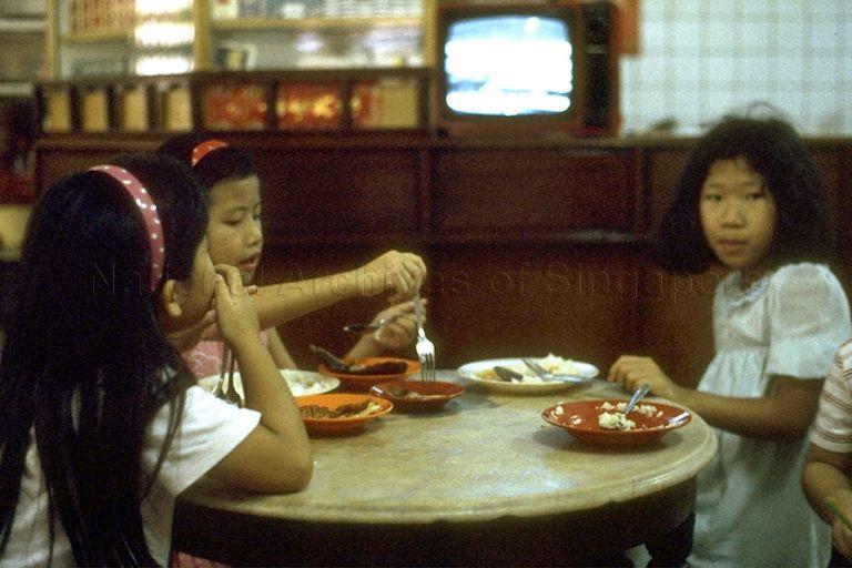 National Day Parade 1985 -- Children watching parade telecast on television while eating dinner
