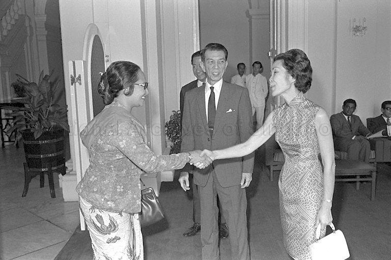 Mrs Benjamin Sheares greeting Mrs Soenarso, wife of Indonesian Ambassador, during morning coffee session in connection with inaugural meeting for 19th annual International Bazaar for the Blind at Istana. Looking on is President Dr Benjamin Henry Sheares.