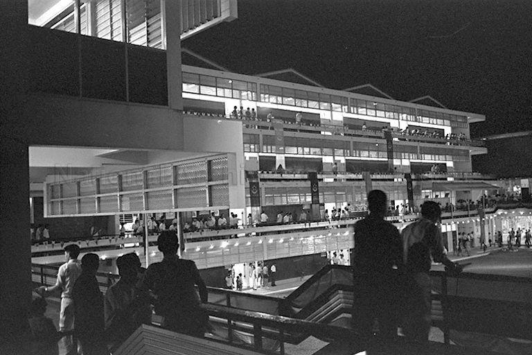 Photo of Broadrick Secondary School taken during the school's opening by Member of Parliament for Katong FJ Conceicao. The new school buildings enclose the ground level assembly area.  This is typical of architectural design for new secondary schools built in post-independence Singapore of 1965. This new design consists of four main buildings, the Teaching Block, the Science and Domestic Science Block, the Assembly Hall, and the Gymnasium which are arranged around a courtyard.  The new design is expected to occupy less space. Better security is also provided by the placement of the four main blocks around a quadrangle.