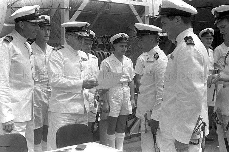 Flag Officer, Malaya, Rear Admiral H J Egerton inspecting a document during handover ceremony of minesweeper HMS Minstrel from British Royal Navy to Royal Siamese Navy, held at Naval Dockyard, Singapore