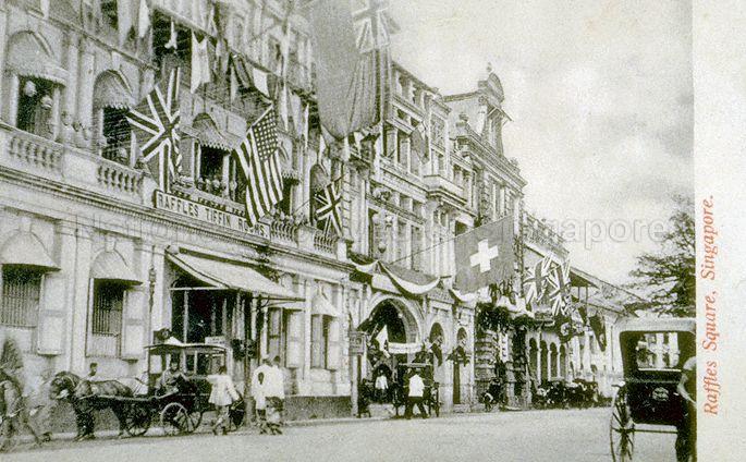 View of Raffles Place, decorated with flags to celebrate coronation of King Edward VII in June. The Raffles Tiffin Rooms, a restaurant run by the Sarkies Brothers who also owned the Raffles Hotel, was a favourite haunt of European merchants.