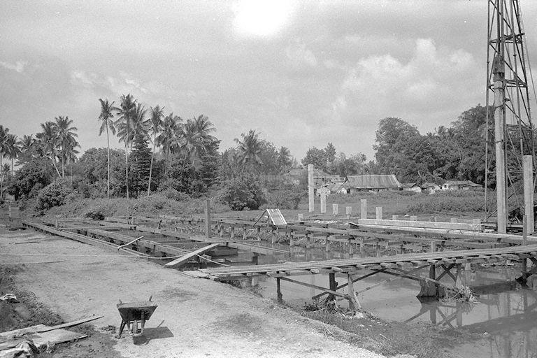 Precast concrete pile being driven by A-frame piling machine beside the canal