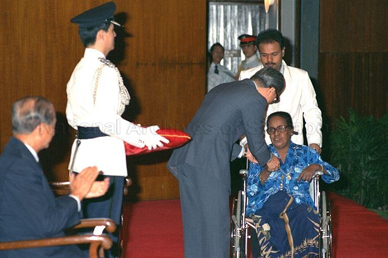 Madam Noorsinah binti Jan receiving the long service medal from Minister for Education Dr Tony Tan. She is rolled upstage in a wheelchair to loud applause from the other recipents and President Wee Kim Wee (left) with the help of her son Abdul Razak bin Mohd Zakaria. The 55-year-old former health attendant with Middle Road Hospital had her right leg amputated due to her diabetic condition two months ago.