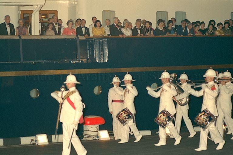Her Majesty Queen Elizabeth II and her guests watching the traditional beating of the retreat performance on the dockside by the Band of Royal Marines from the royal yacht, HMY Britannia during the return banquet hosted by the Queen