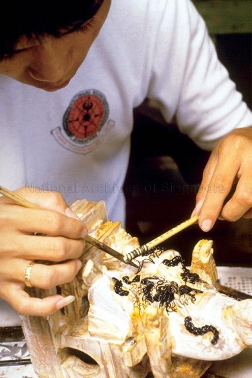 Man carving wooden deity statue at "Say Tian Kok", 19 Club Street, a shop owned by Ng Yew Kian