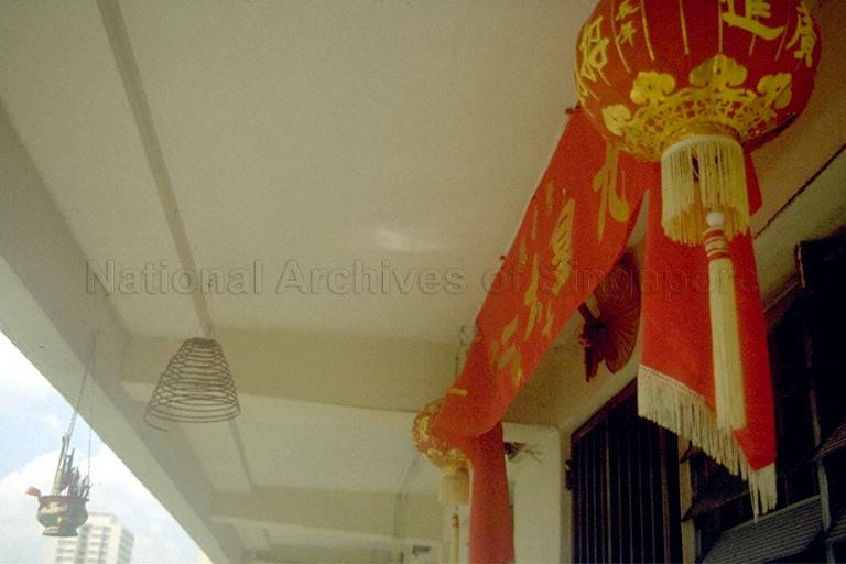 A Taoist banner, lantern, spiral incense coil and incense pot outside a Housing and Development Board (HDB) flat