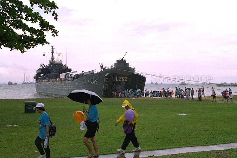 Visitors walking in the rain during the Singapore Carnival cum Community Day and launch of National Healthy Lifestyle campaign at East Coast Park. In the background is Republic of Singapore Navy Landing Ship Tank (LST) RSS Excellence L202, beached next to Bedok Jetty.