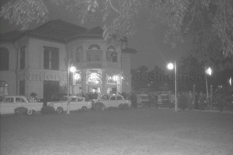 View of guests and cars parked outside Mandalay Villa, No. 29 Amber Road, during birthday celebration for Madam Tan Teck Neo. Built in 1902 as a holiday resort by prominent Peranakan businessman Lee Cheng Yan, the beautiful seaside bungalow was designed by Lermit & Westerhout. It later became residence of his son Lee Choon Guan and his wife, Madam Tan, who lived here with her family until she passed away in February 1978. With its fanciful facade, it was well known for parties thrown by Madam Tan, which brought the Chinese and British communities together in those days when they seldom mixed.
