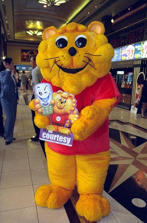 Singa the Courtesy Lion, mascot for Courtesy Campaign, holding poster showing this year's theme "Let's use handphones with courtesy" during launch of 22nd National Courtesy Campaign at Golden Village Grand cinema complex, Great World City