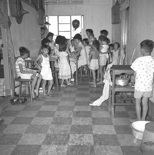 Women and children staying home in Chinatown during curfew hours. They are probably tenants renting rooms in a shophouse, which was common before establishment of the Housing and Development Board (HDB) in 1960. Curfew was imposed for about ten days by the British colonial government at height of unrest caused by students and members of the Singapore Chinese Middle Schools Students' Union (SCMSSU) protesting against decision to dissolve the SCMSSU as a communist-front organisation and subsequent dismissal of teachers and students who had participated in subversive activities.