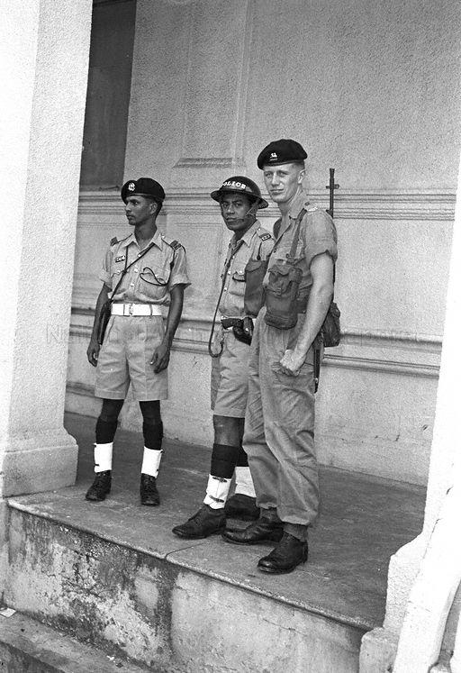 View of policemen, the one in the middle donning uniform of riot police, and British military personnel patrolling Chinatown where students and members of the Singapore Chinese Middle Schools Students' Union (SCMSSU) had barricaded themselves in a building. The group had earlier marched in from Chinese High School in Bukit Timah, one of two schools (the other being Chung Cheng High School) where some 4 000 students had stage a stay-in protest strike since 10 October against the government's decision to dissolve the SCMSSU as a communist-front organisation and the subsequent dismissal of teachers and students who had participated in subversive activities. The tension culminated into rioting outside Chinese High School on 25 October and at dawn the next day, the police cleared the school with tear-gas. The students then began to march into the city area.