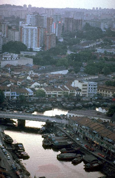 Aerial view of Singapore River and Read Bridge, with Clarke Quay in the foreground and high-rise flats in the background. Twakows are parked against the river's banks.