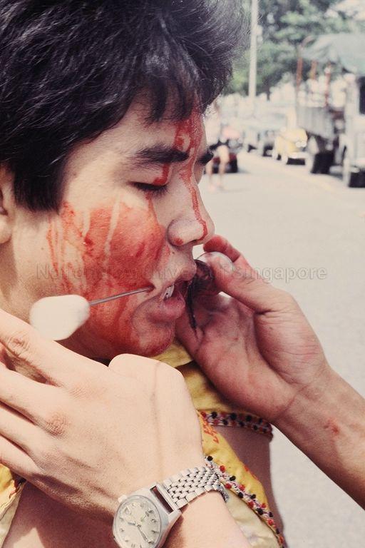 "Kwan Kong" birthday celebration at Delta Road Housing and Development Board (HDB) estate -- Close-up of medium, with his face smeared with blood, being pierced with spikes in preparation for procession organised by the Delta Road temple