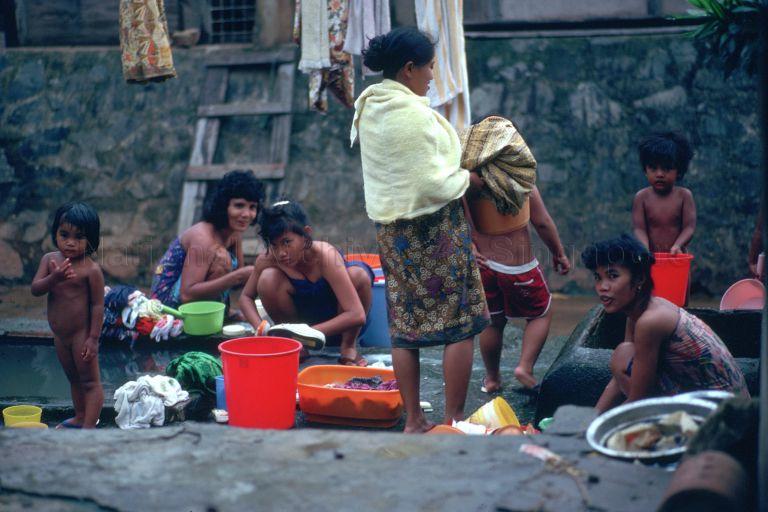 Women washing clothes and children bathing using underground water from 'well' dug by dwellers of the Cherry Tree Mosque kampong at Pepys Road