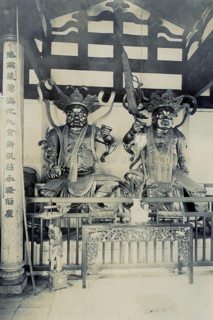 Statues of two of The Four Heavenly Kings in the Hall of the Devas at Kek Lok Si Temple, Ayer Itam, Penang, Malaya. The Four Heavenly Kings are Buddhist deities who guard each of the four points on the compass. Holding a snake in his hand, the Guardian of the West (left) is Kuang Mu Tian Wang whose name suggests "The One with Broad Perception". Guardian of the North, Duo Wen Tian Wang (right), holds an umbrella.