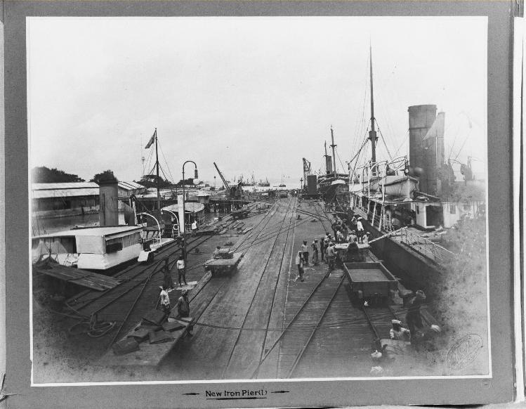 Penang Harbour. New iron pier. Close-up view of ships and labourers loading ship with sacks